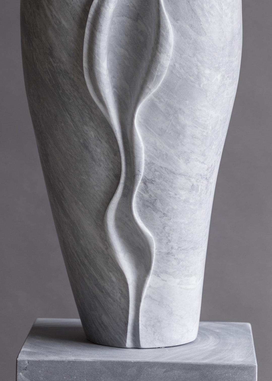 Tall contemporary sculpture hand-carved from pale Italian marble, featuring an elegant elongated form with flowing, organic curves and soft wave-like lines, poised on a smooth stone plinth with a serene, modern presence.