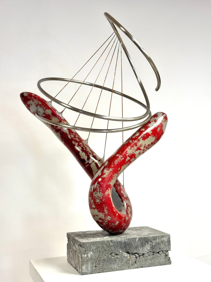 Abstract mixed media sculpture with looping red and silver marbled GRP form, intersected by brushed stainless steel rings and fine rust-treated steel strands, mounted on a grey stone base. Contemporary one-off artwork by Mark Purllant.