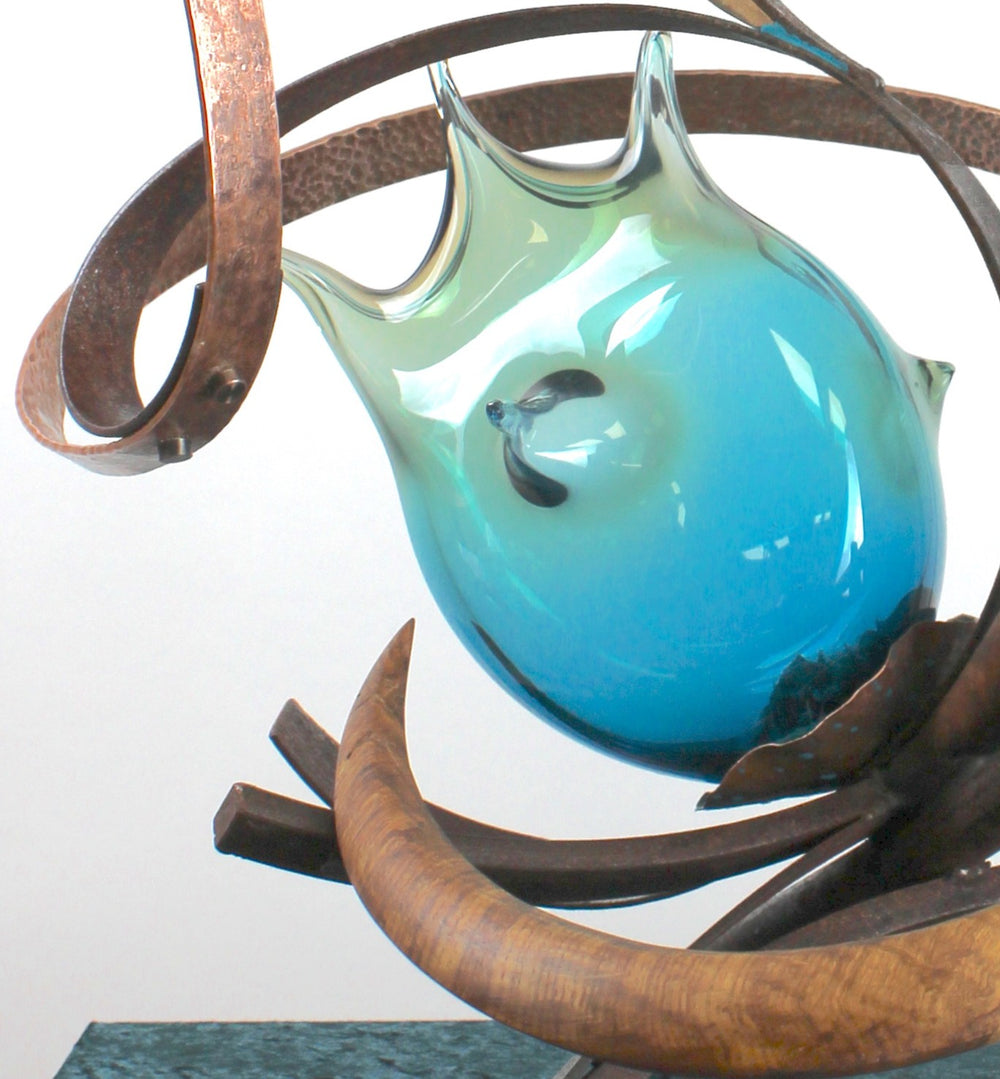 Pod by Mark Purllant, a one-off mixed media sculpture combining carved English brown oak, rust-treated steel, and hand-blown glass in vivid sea green and blue tones, accented with hand-beaten copper and organic flowing forms.