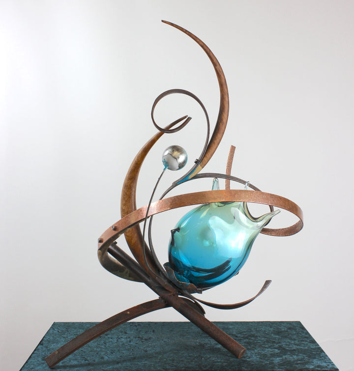 Pod by Mark Purllant, a one-off mixed media sculpture combining carved English brown oak, rust-treated steel, and hand-blown glass in vivid sea green and blue tones, accented with hand-beaten copper and organic flowing forms.