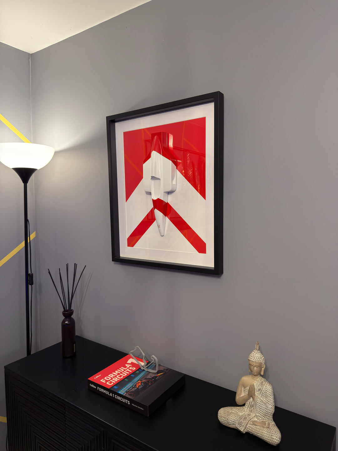 ‘McLaren MP4/4 Inspired Wall Art’ by Srini Gandra, a limited-edition contemporary automotive wall sculpture from the ICONS on The Wall series, celebrating Ayrton Senna and the legendary McLaren MP4/4 Formula 1 racing car. Handcrafted from resin and finished in high-gloss automotive paint, the three-dimensional sculpture features a streamlined white racing car viewed from above, with red detailing and the number 12 on its nose. Mounted against a bold red and white geometric background within a black wooden d