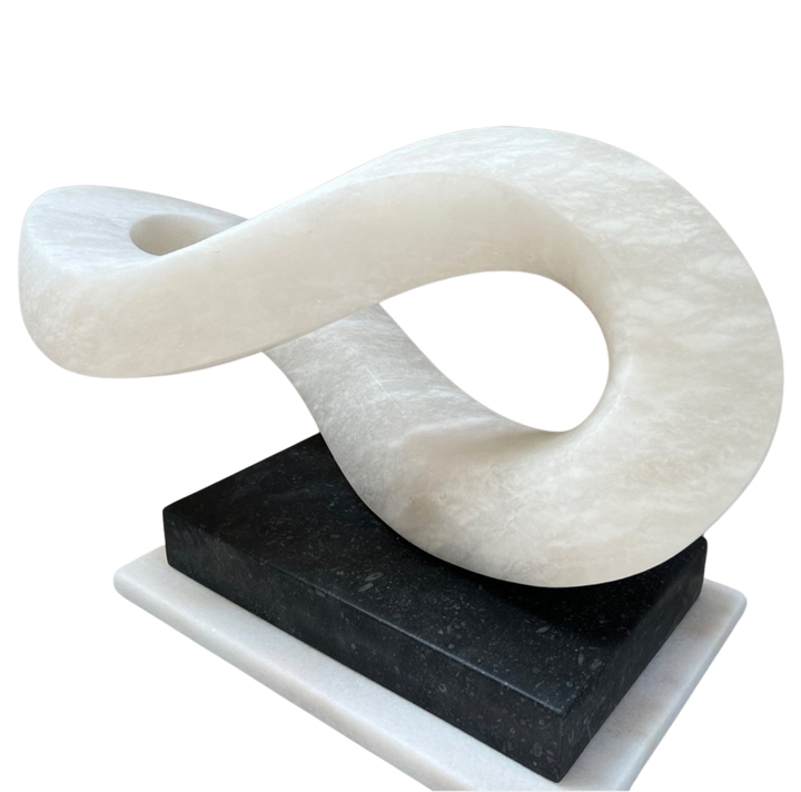 Abstract alabaster sculpture Meander – 2024 by Hamish Holman, hand-carved from Spanish alabaster into a fluid looping infinity-like form with soft translucent white tones, displayed on a contrasting dark stone base.