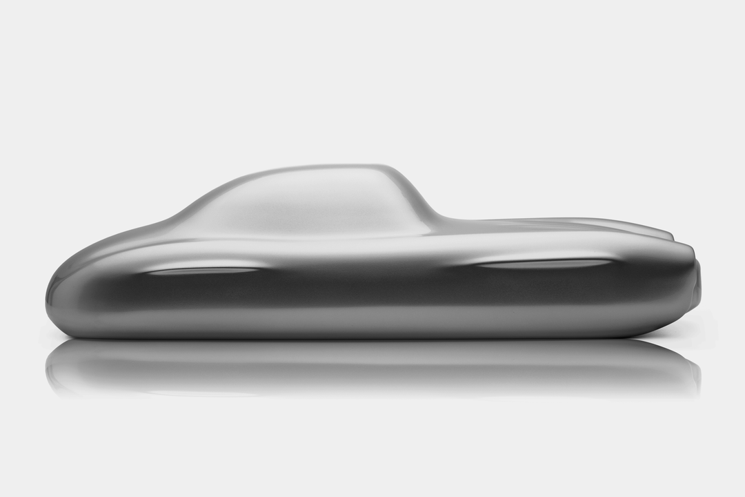‘Mercedes 300SL’ by Srini Gandra, a limited-edition contemporary automotive sculpture from the Forme di Velocità series, inspired by the iconic Mercedes-Benz 300 SL Gullwing. Presented in an elegant Silver Grey metallic finish, the sculpture captures the classic sports car's elongated bonnet, distinctive rounded front wings, low-slung body, sculpted side contours and gracefully curved roofline. Its smooth, minimalist surfaces celebrate the aerodynamic elegance, timeless proportions and pioneering design of 