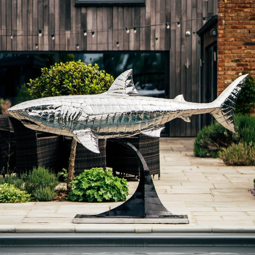 ‘Great White’ by Michael Turner, a unique, one-of-one stainless steel marine wildlife sculpture depicting a powerful great white shark swimming with its mouth partially open, exposing rows of sharp triangular teeth. Handcrafted from intricately shaped and welded stainless steel, the sculpture features a polished silver finish, detailed metallic skin, distinctive dorsal and pectoral fins and a sweeping tail. Mounted on a curved black metal support with a rectangular base, this large-scale contemporary sculpt