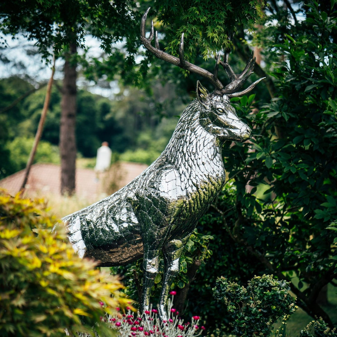 ‘Royal Stag’ by Michael Turner, a unique, one-of-one stainless steel wildlife sculpture depicting a majestic red deer stag standing proudly with an impressive set of 12-point antlers. Handcrafted from marine-grade stainless steel, the life-size sculpture features individually shaped metallic plates, finely detailed fur textures, powerful muscular proportions and a polished silver finish that reflects its natural surroundings. Designed for outdoor display, this contemporary British wildlife sculpture capture