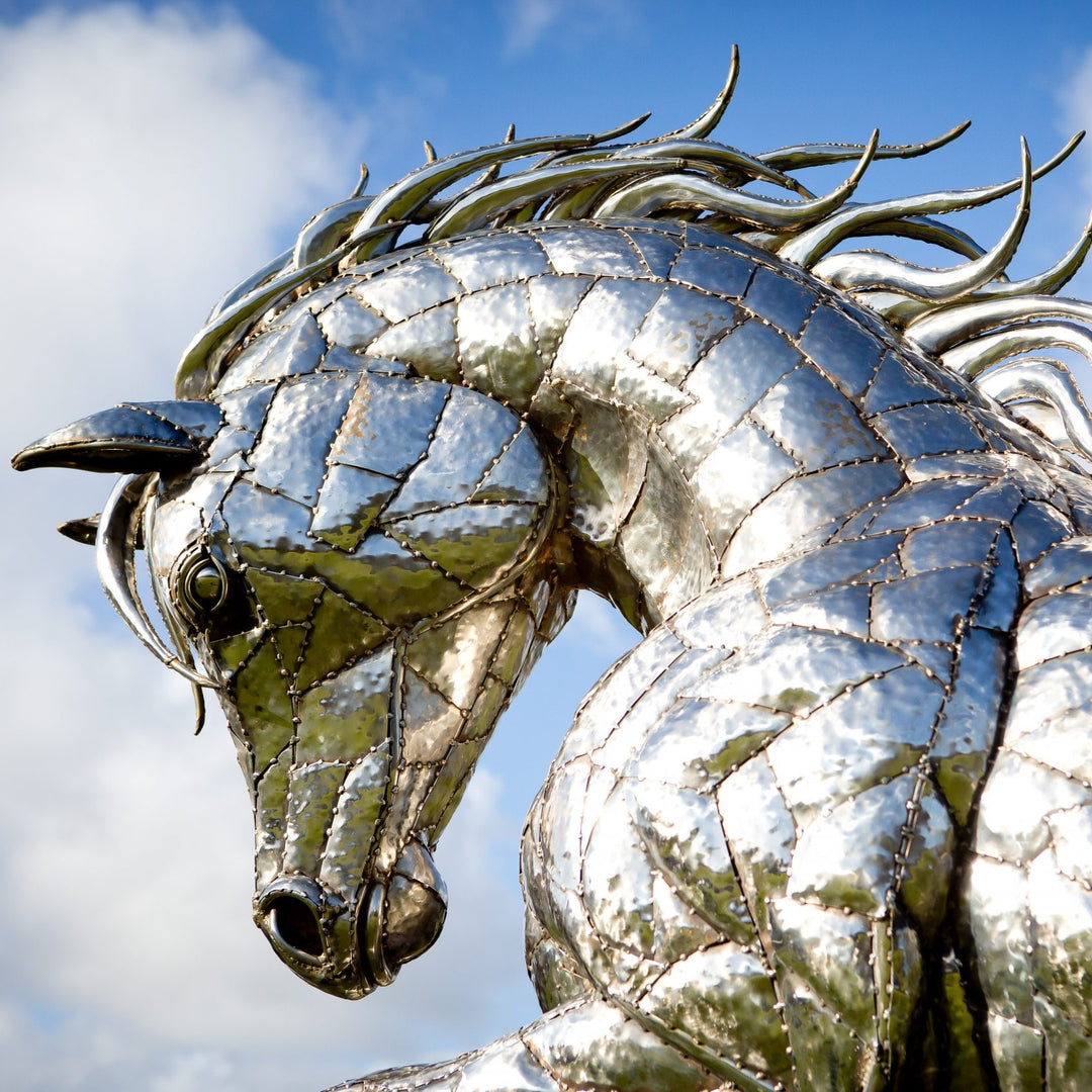 ‘Leaping Horse’ by Michael Turner, a unique, one-of-one stainless steel equestrian sculpture depicting a magnificent life-size horse leaping forward with its front legs raised and hind legs extended. Handcrafted from marine-grade stainless steel, the sculpture features intricately welded metallic plates, a powerful muscular body, flowing mane and sweeping tail. Its polished silver finish reflects the surrounding landscape, while the dynamic pose captures the strength, elegance and movement of a horse in ful