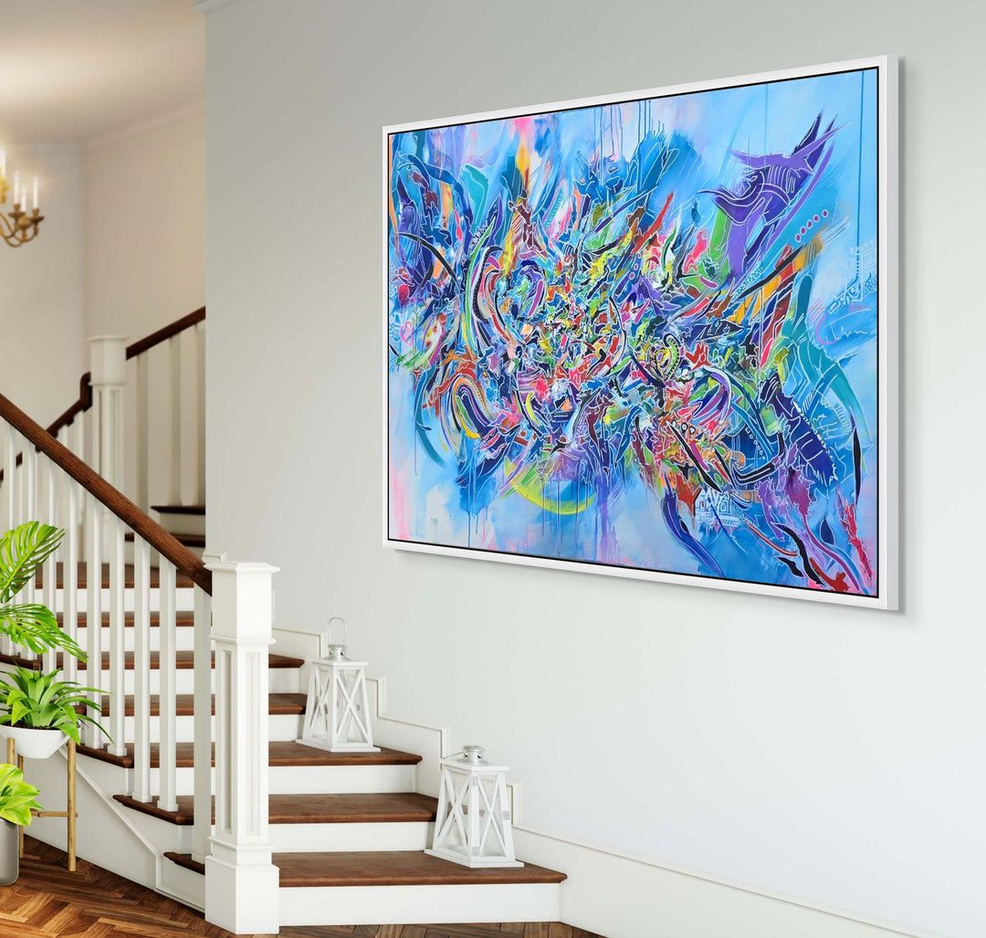Vibrant large-scale abstract graffiti painting bursting with layered colour, bold sweeping lines and dynamic shapes against a bright blue background, framed in a white tray frame.