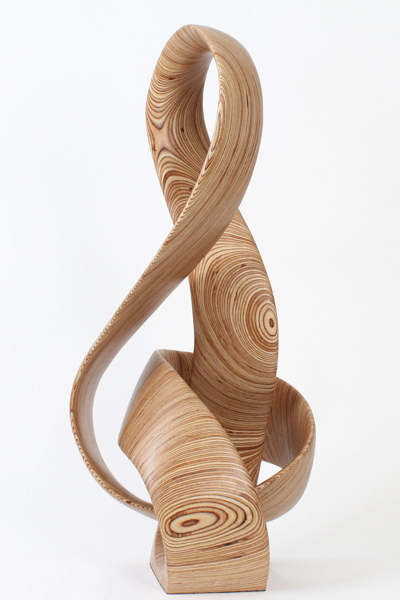 Hand-carved birch plywood sculpture by Bill Prickett combining a treble clef and Möbius strip into a continuous, flowing form, with layered wood grain revealing an infinity loop inspired by music and mathematics.