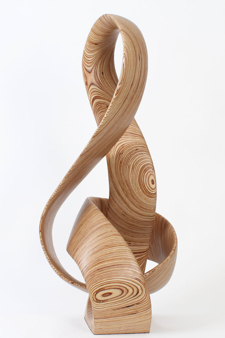 Hand-carved birch plywood sculpture by Bill Prickett combining a treble clef and Möbius strip into a continuous, flowing form, with layered wood grain revealing an infinity loop inspired by music and mathematics.