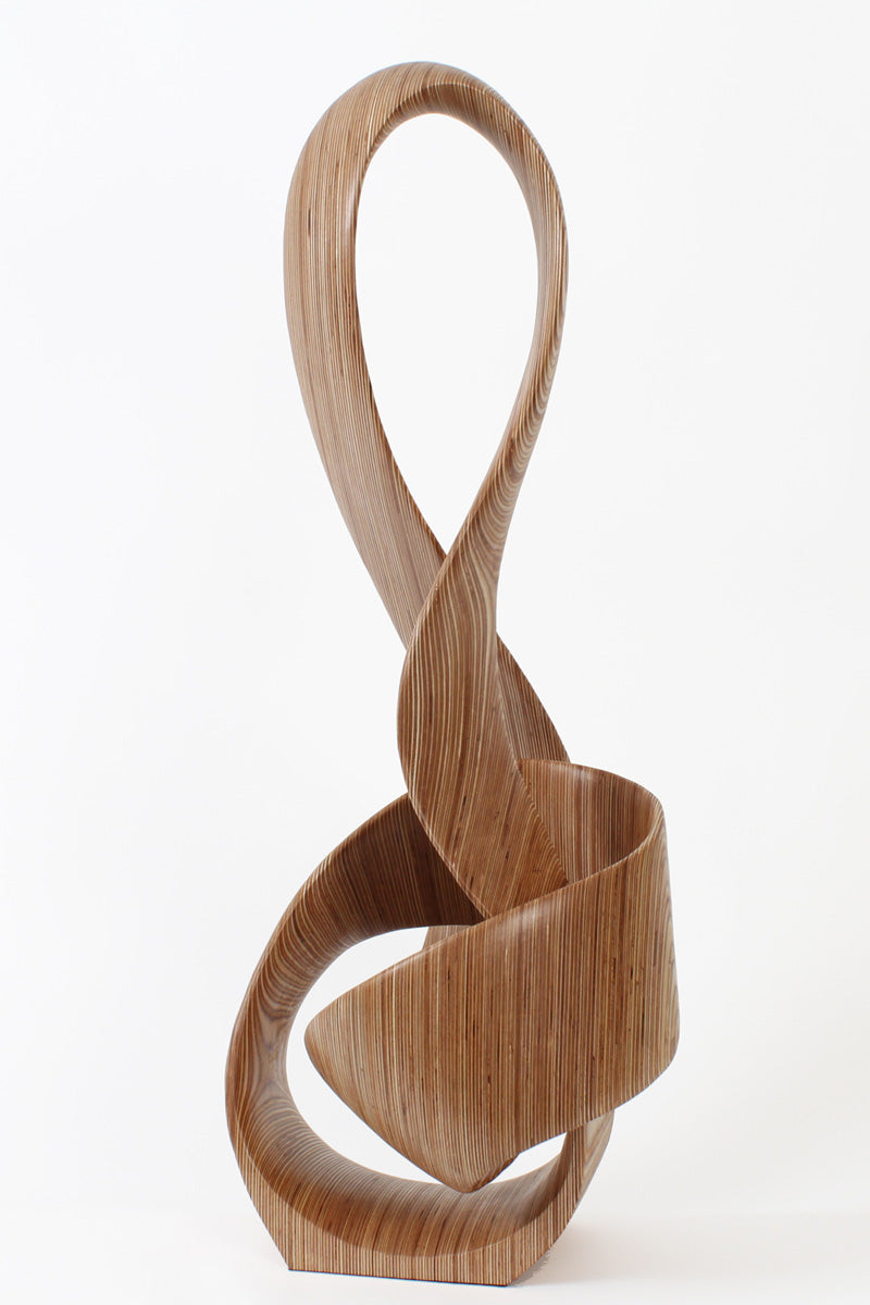 Hand-carved birch plywood sculpture by Bill Prickett combining a treble clef and Möbius strip into a continuous, flowing form, with layered wood grain revealing an infinity loop inspired by music and mathematics.