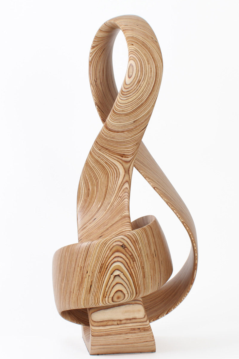 Hand-carved birch plywood sculpture by Bill Prickett combining a treble clef and Möbius strip into a continuous, flowing form, with layered wood grain revealing an infinity loop inspired by music and mathematics.
