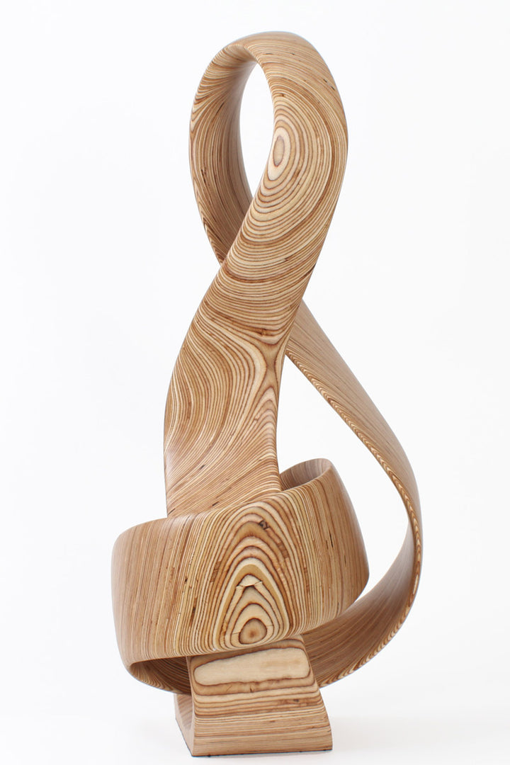 Hand-carved birch plywood sculpture by Bill Prickett combining a treble clef and Möbius strip into a continuous, flowing form, with layered wood grain revealing an infinity loop inspired by music and mathematics.