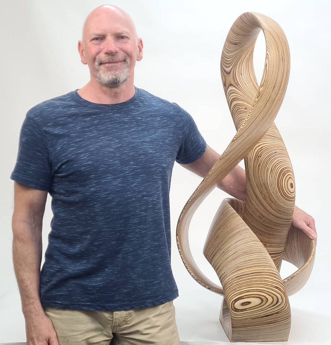 Hand-carved birch plywood sculpture by Bill Prickett combining a treble clef and Möbius strip into a continuous, flowing form, with layered wood grain revealing an infinity loop inspired by music and mathematics.