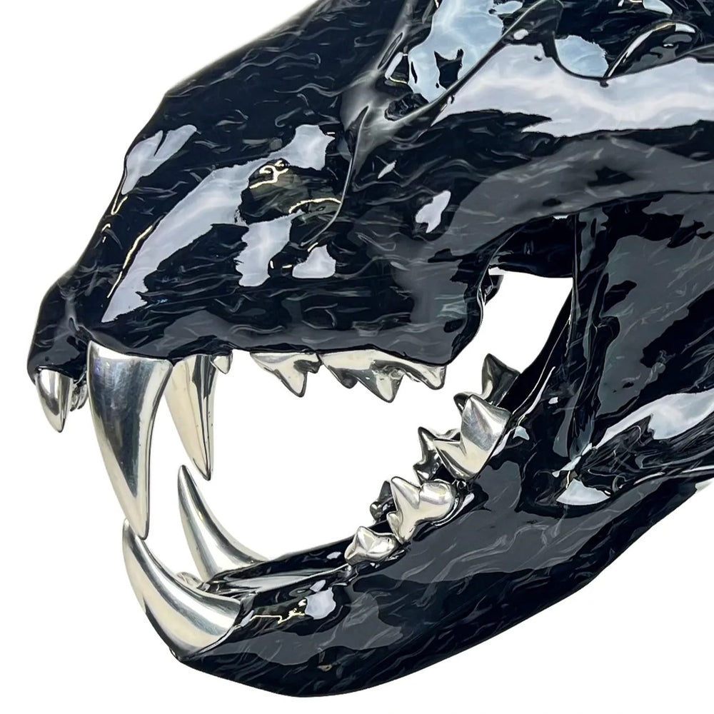 A striking, polished carbon fibre lion skull sculpture by Alastair Gibson, crafted with Mokume-style carbon layup for a swirling, chaotic texture. The jaw is fitted with gleaming bismuth alloy teeth. Mounted on a genuine F1 gearbox selector barrel atop a granite base, the work merges natural form with elite motorsport engineering.