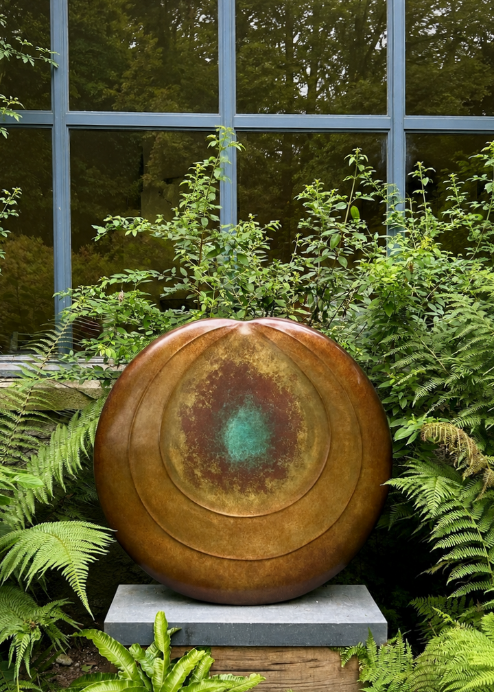 Circular bronze sculpture by Dominic Welch, Aurorean Moon, featuring a layered, concentric form with a glowing turquoise-green patina at its centre, radiating outwards into rich bronze and earthy red-gold tones. A refined limited-edition work blending celestial inspiration with organic presence.