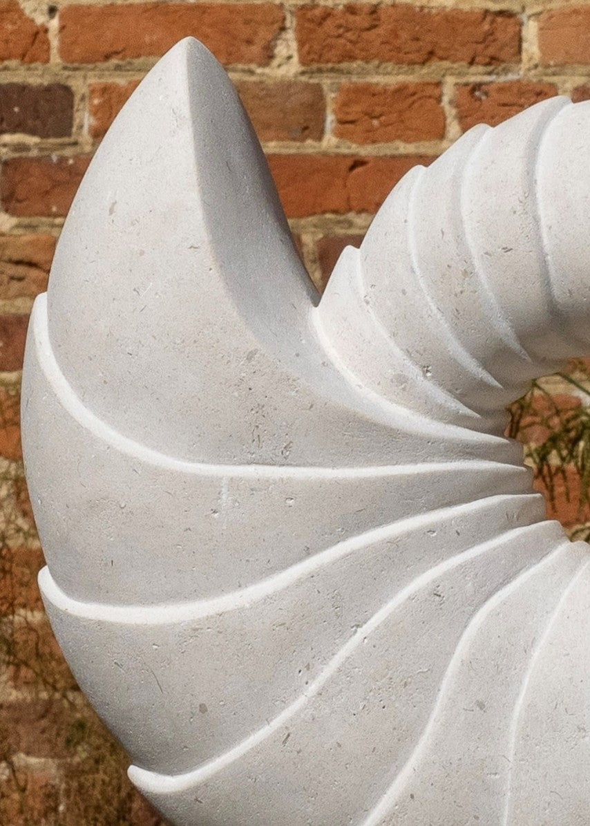 Nautilus by Nicola Axe — elegant spiral Portland stone sculpture echoing a seashell’s natural form, smooth pale surface with flowing ridges, mounted on a granite and oak plinth with a discreet metal plate.
