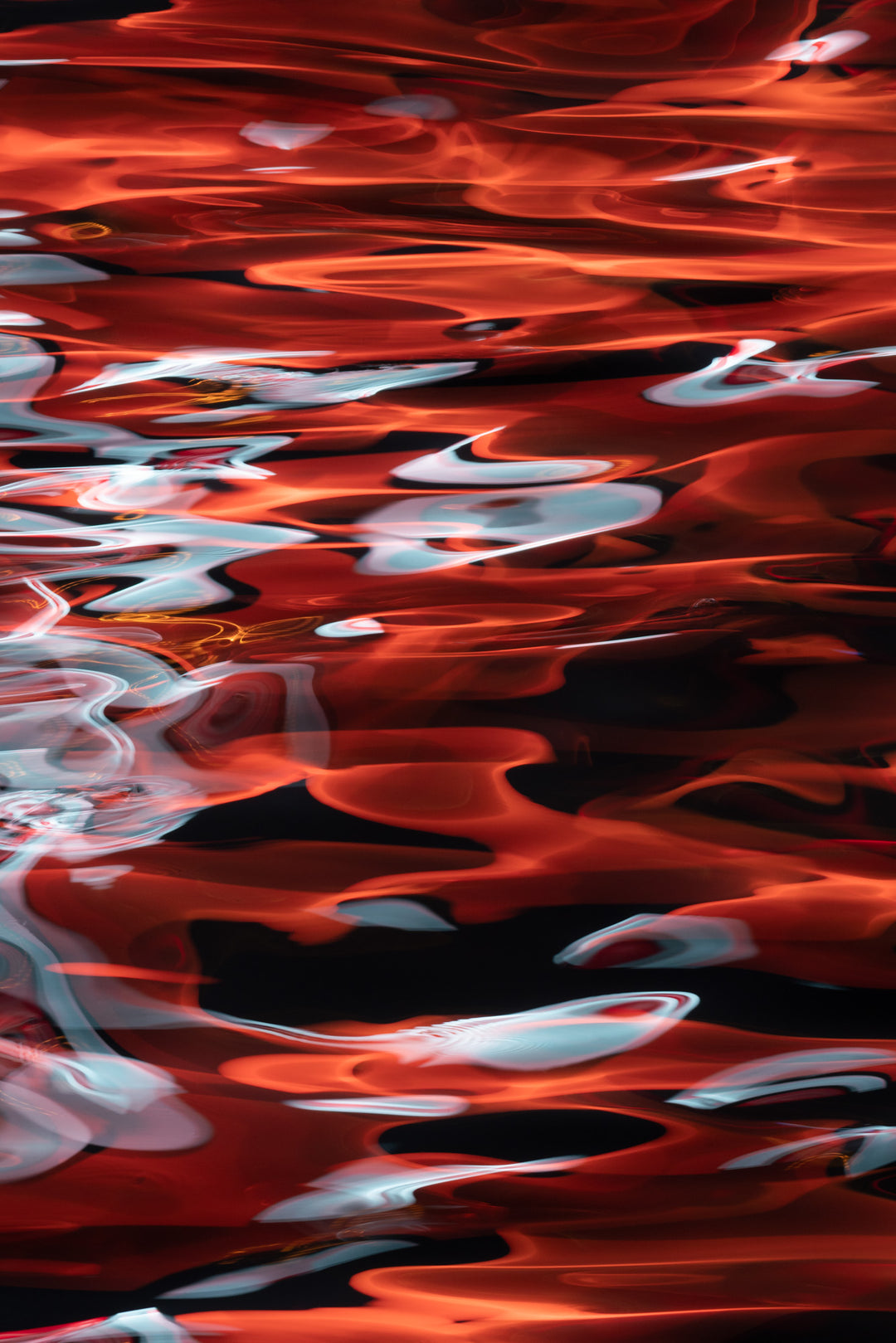 Abstract photograph capturing vivid red and white light reflections on the surface of water at night, with flowing, flame-like patterns and a dramatic sense of movement.
