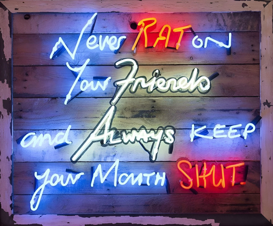 Neon wall art by Matthew Bracey featuring the iconic mob quote “Never RAT on your friends and always keep your mouth SHUT.” The words are written in bold neon script across a distressed wood panel in red, blue, white, yellow, and orange neon colours, creating a striking and rebellious visual statement.