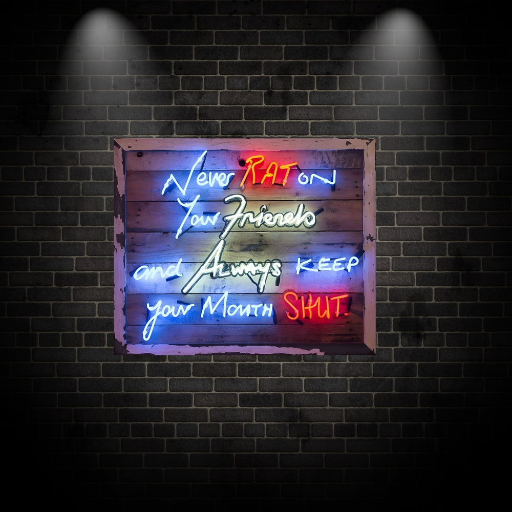 Neon wall art by Matthew Bracey featuring the iconic mob quote “Never RAT on your friends and always keep your mouth SHUT.” The words are written in bold neon script across a distressed wood panel in red, blue, white, yellow, and orange neon colours, creating a striking and rebellious visual statement.