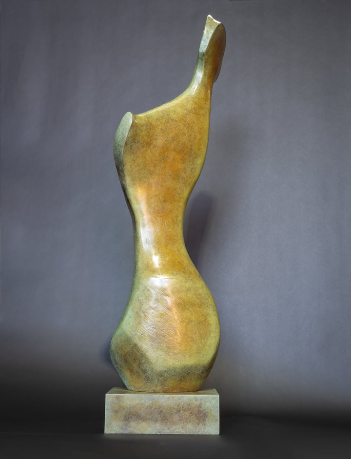 Bone Form IV — abstract bronze sculpture by Nicola Godden inspired by the natural curves and hollows of animal bone. The piece has a tall, sinuous form with a hollowed centre, organic surface texture and warm bronze patina shifting from earthy brown to soft green and gold highlights. Displayed outdoors on a one-metre timber plinth against a bright blue sky and winter landscape.