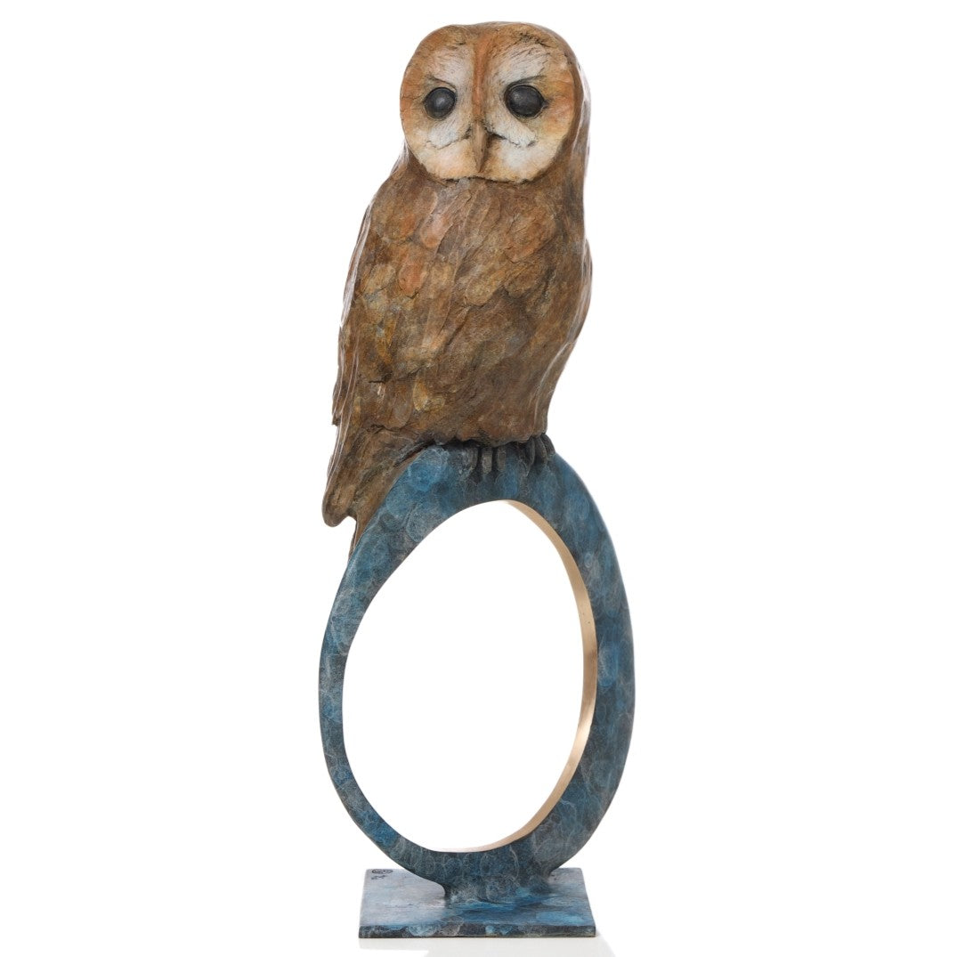 ‘Nocturne’ by Pat Bull, a limited-edition contemporary bronze wildlife sculpture depicting a tawny owl perched on top of a large upright circular bronze ring. The owl features a rounded, heart-shaped facial disc in cream and warm beige, prominent dark eyes and detailed feathers finished in earthy brown and bronze tones. The open ring features a mottled turquoise, teal and blue-green patina with a contrasting polished golden inner edge, mounted on a small rectangular bronze base against a white background.