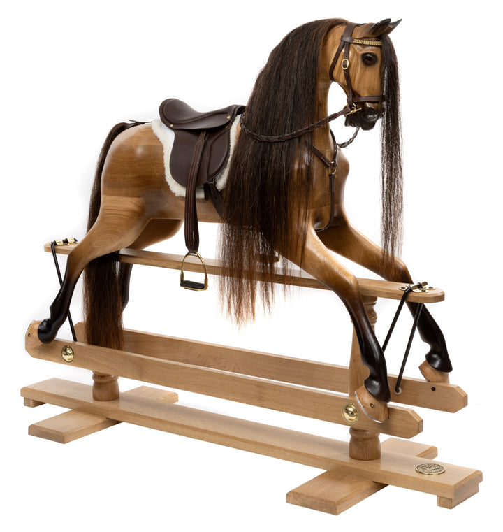 Handcrafted wooden rocking horse, with dark leather saddle and bridle, set against a white background.