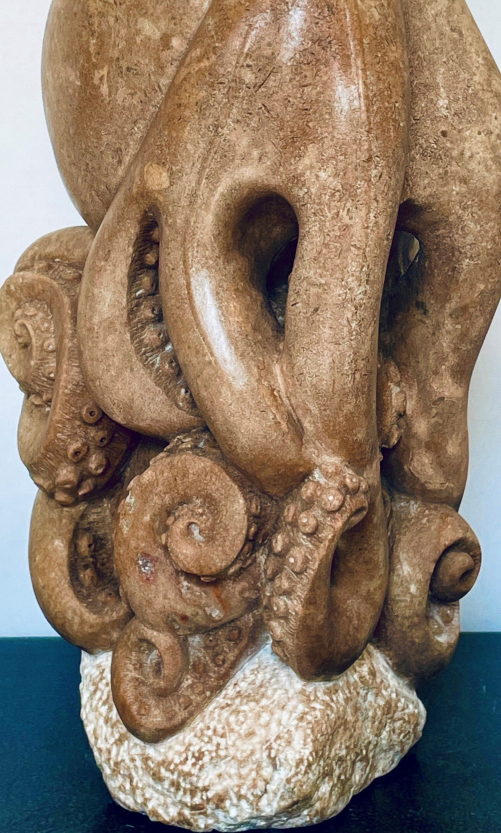 Octopus sculpture by Nicola Axe — intricately carved from warm pink serpentine, with coiled curling tentacles and smooth rounded head, perched on a pale textured stone base, blending marine life detail with organic elegance.