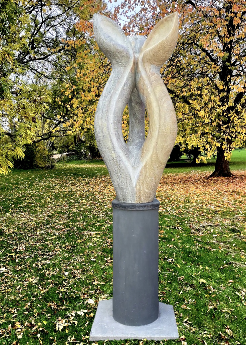 Offspring by Martin Cash — a hand-carved Ancaster Weatherbed stone sculpture mounted on a granite base. The tall, abstract form features two intertwined organic shapes, symbolising growth and unity, designed for display in gardens or public spaces.