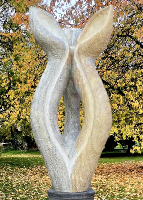 Offspring by Martin Cash — a hand-carved Ancaster Weatherbed stone sculpture mounted on a granite base. The tall, abstract form features two intertwined organic shapes, symbolising growth and unity, designed for display in gardens or public spaces.