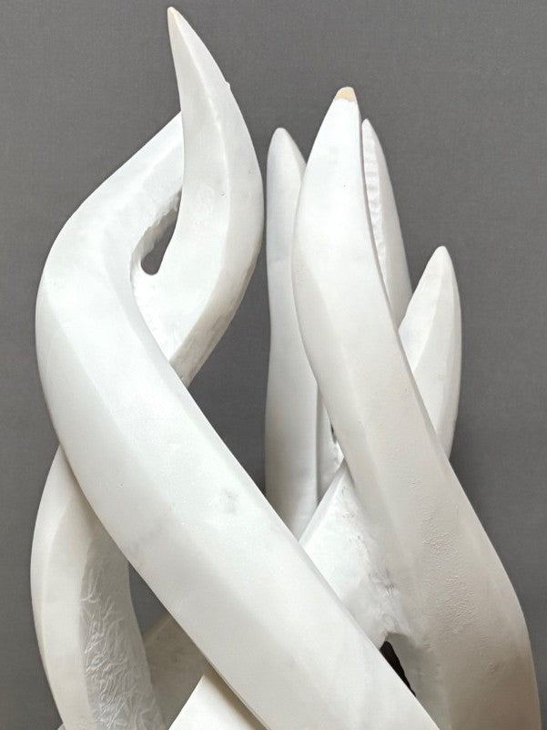 Once More by Brendan Cullen, a dynamic hand-carved sculpture in Carrara marble, formed of interlacing, flame-like ribbons that twist upward in fluid motion. The smooth white marble is contrasted with textured inner surfaces, giving depth and vitality to the piece. Mounted on a dark stone base, it captures a sense of energy, renewal, and continuous flow.