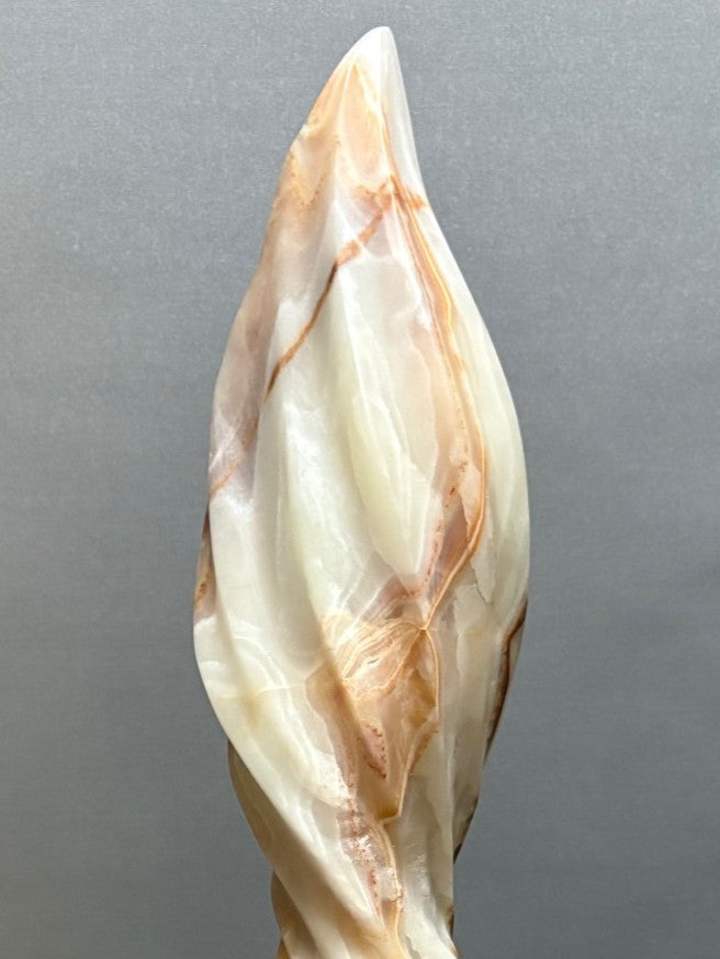 Onyx Twist by Brendan Cullen, a hand-carved Patagonian onyx sculpture with a slender, flame-like spiral form rising from a rounded wooden base, the translucent stone glowing in creamy white with warm amber and rust-coloured veining.