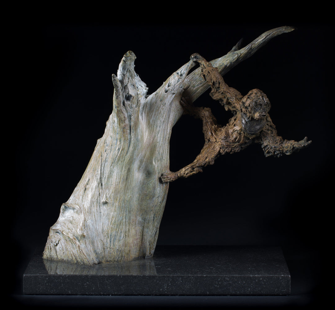 Bronze sculpture of a gibbon leaping from a sculpted tree trunk, mounted on a polished black base against a dark background