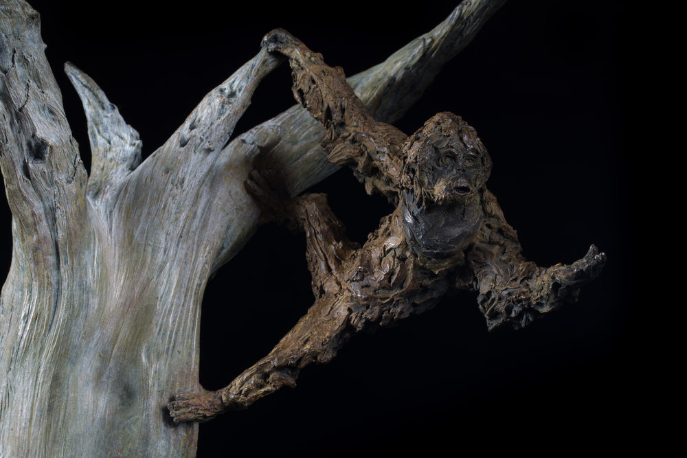 Bronze sculpture of a gibbon leaping from a sculpted tree trunk, mounted on a polished black base against a dark background