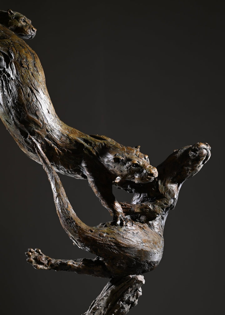 ‘Otters Playing Underwater’ by Hamish Mackie, a life-size limited-edition bronze wildlife sculpture depicting a mother otter and her playful cubs twisting, diving and swimming around a sculpted underwater tree root. The dynamic vertical composition features expressive animal movements, detailed fur textures and a weathered bronze finish in rich brown and earthy tones, capturing the playful energy and natural behaviour of otters beneath the water.