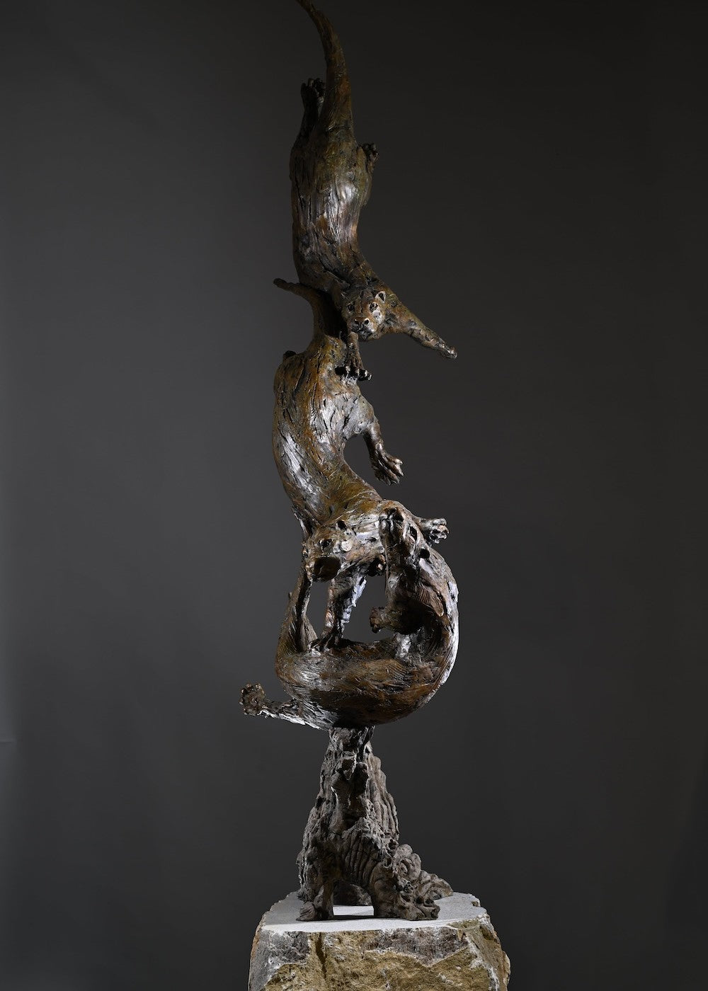 ‘Otters Playing Underwater’ by Hamish Mackie, a life-size limited-edition bronze wildlife sculpture depicting a mother otter and her playful cubs twisting, diving and swimming around a sculpted underwater tree root. The dynamic vertical composition features expressive animal movements, detailed fur textures and a weathered bronze finish in rich brown and earthy tones, capturing the playful energy and natural behaviour of otters beneath the water.