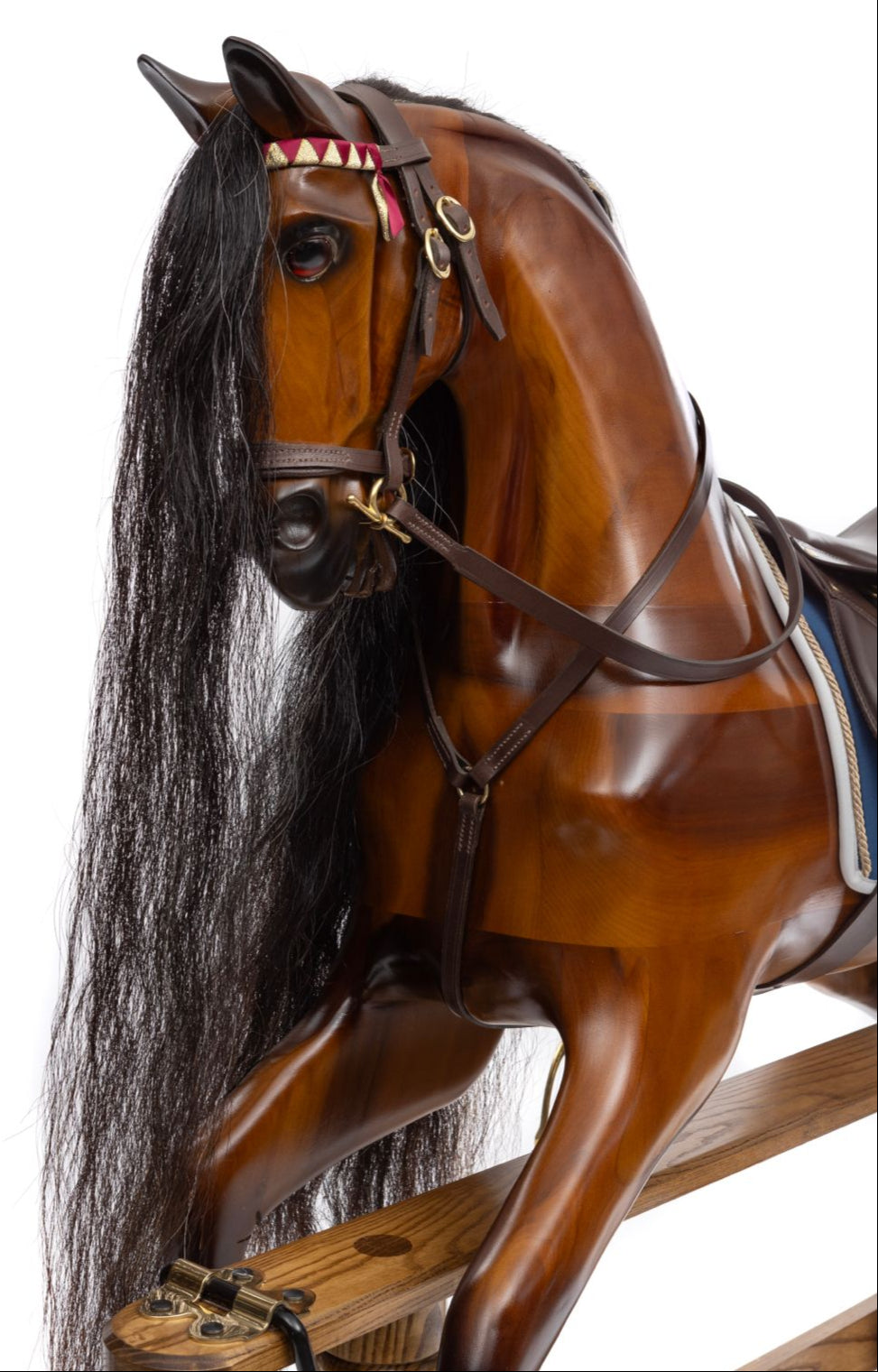 Polished wooden rocking horse with dark mane, blue saddle cloth, and leather tack, displayed on an oak safety stand.

