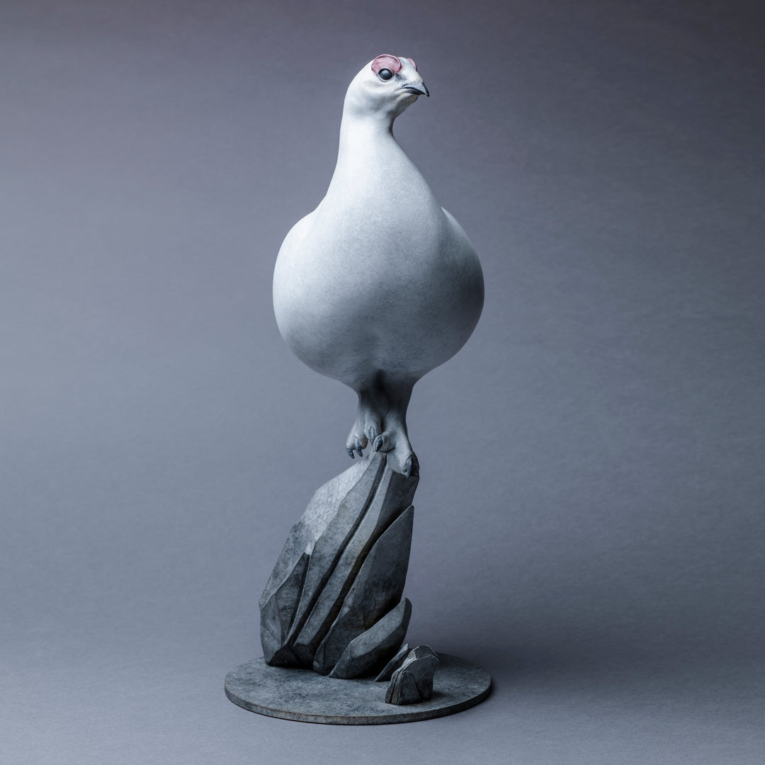 A finely sculpted Nick Bibby bronze ptarmigan standing tall on an angular rocky base, with a smooth winter-white patina and soft grey tonality, capturing the bird’s alert posture and clean, rounded form against a neutral backdrop.