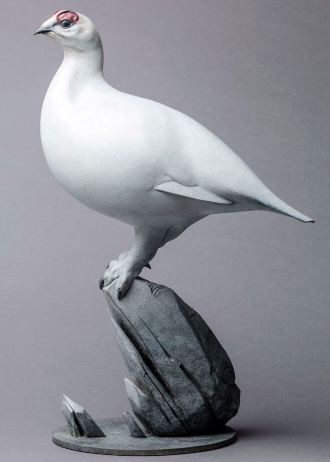 A finely sculpted bronze ptarmigan standing tall on an angular rocky base, with a smooth winter-white patina and soft grey tonality, capturing the bird’s alert posture and clean, rounded form against a neutral backdrop.