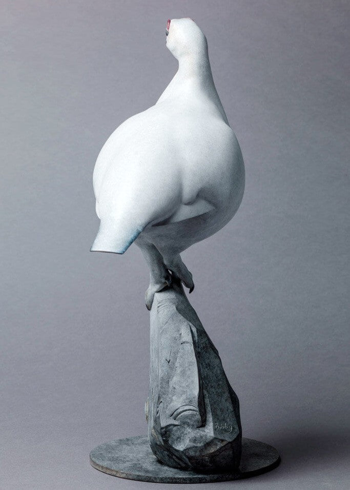 A finely sculpted bronze ptarmigan standing tall on an angular rocky base, with a smooth winter-white patina and soft grey tonality, capturing the bird’s alert posture and clean, rounded form against a neutral backdrop.