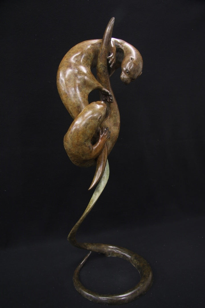 Elegant bronze sculpture of two otters playfully entwined in an upward spiral against a black background.