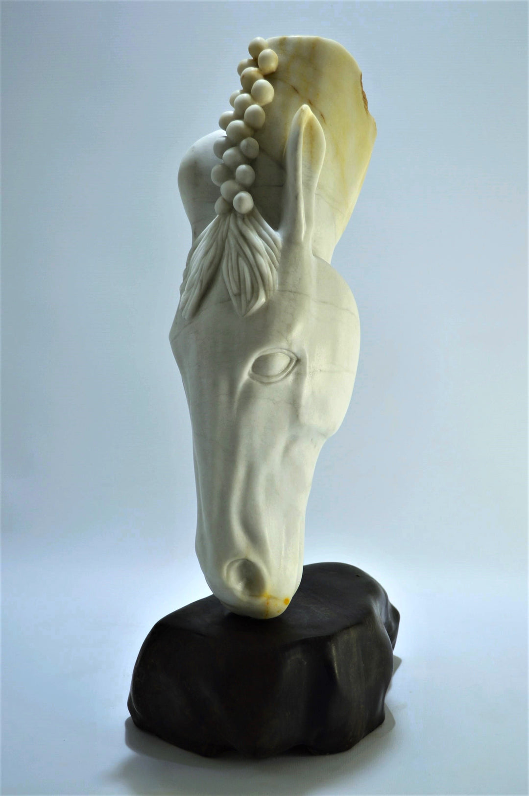 Deborah Harrison sculpture Palomo, a one-off hand-carved horse head in rainbow alabaster with intricate mane detail and a natural crown of rounded alabaster spheres, mounted on a dark soapstone base. The alabaster reveals soft white, ivory, cream and golden brown tones with darker natural veining, blending realism with symbolic form.