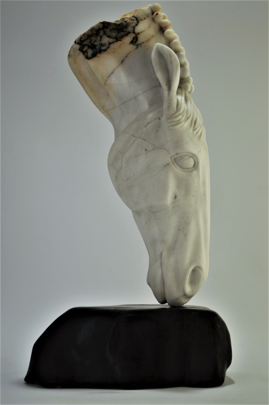 Deborah Harrison sculpture Palomo, a one-off hand-carved horse head in rainbow alabaster with intricate mane detail and a natural crown of rounded alabaster spheres, mounted on a dark soapstone base. The alabaster reveals soft white, ivory, cream and golden brown tones with darker natural veining, blending realism with symbolic form.