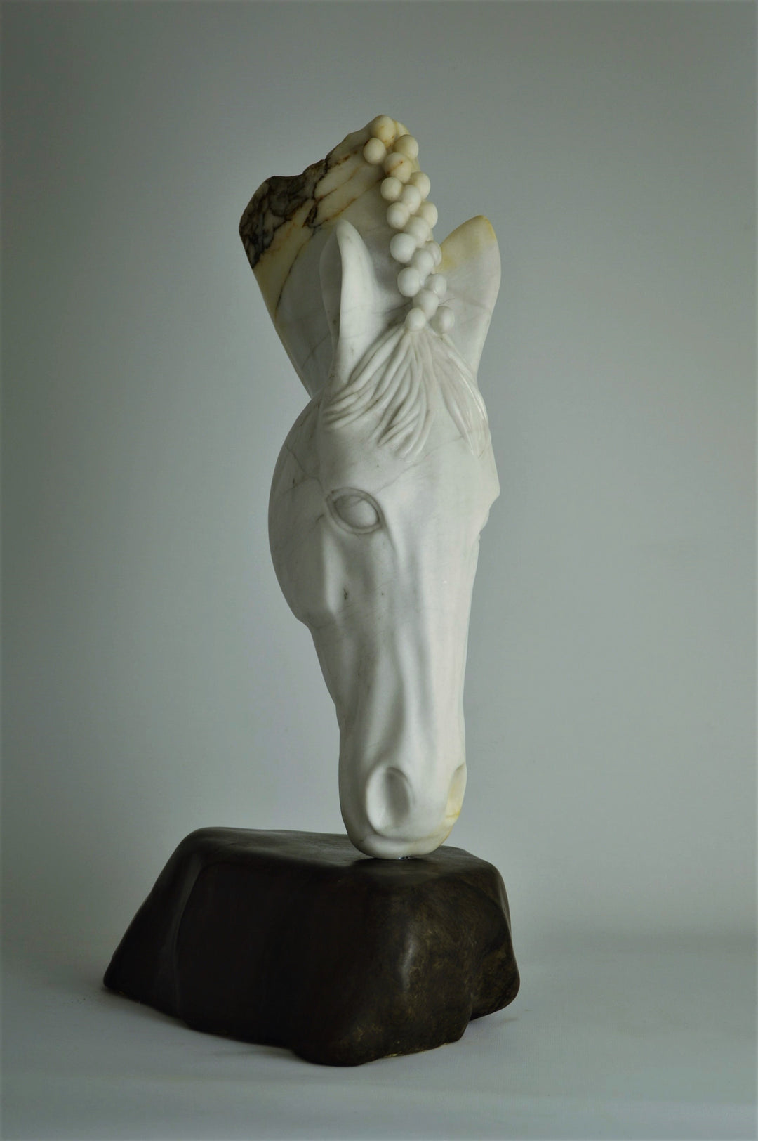 Deborah Harrison sculpture Palomo, a one-off hand-carved horse head in rainbow alabaster with intricate mane detail and a natural crown of rounded alabaster spheres, mounted on a dark soapstone base. The alabaster reveals soft white, ivory, cream and golden brown tones with darker natural veining, blending realism with symbolic form.