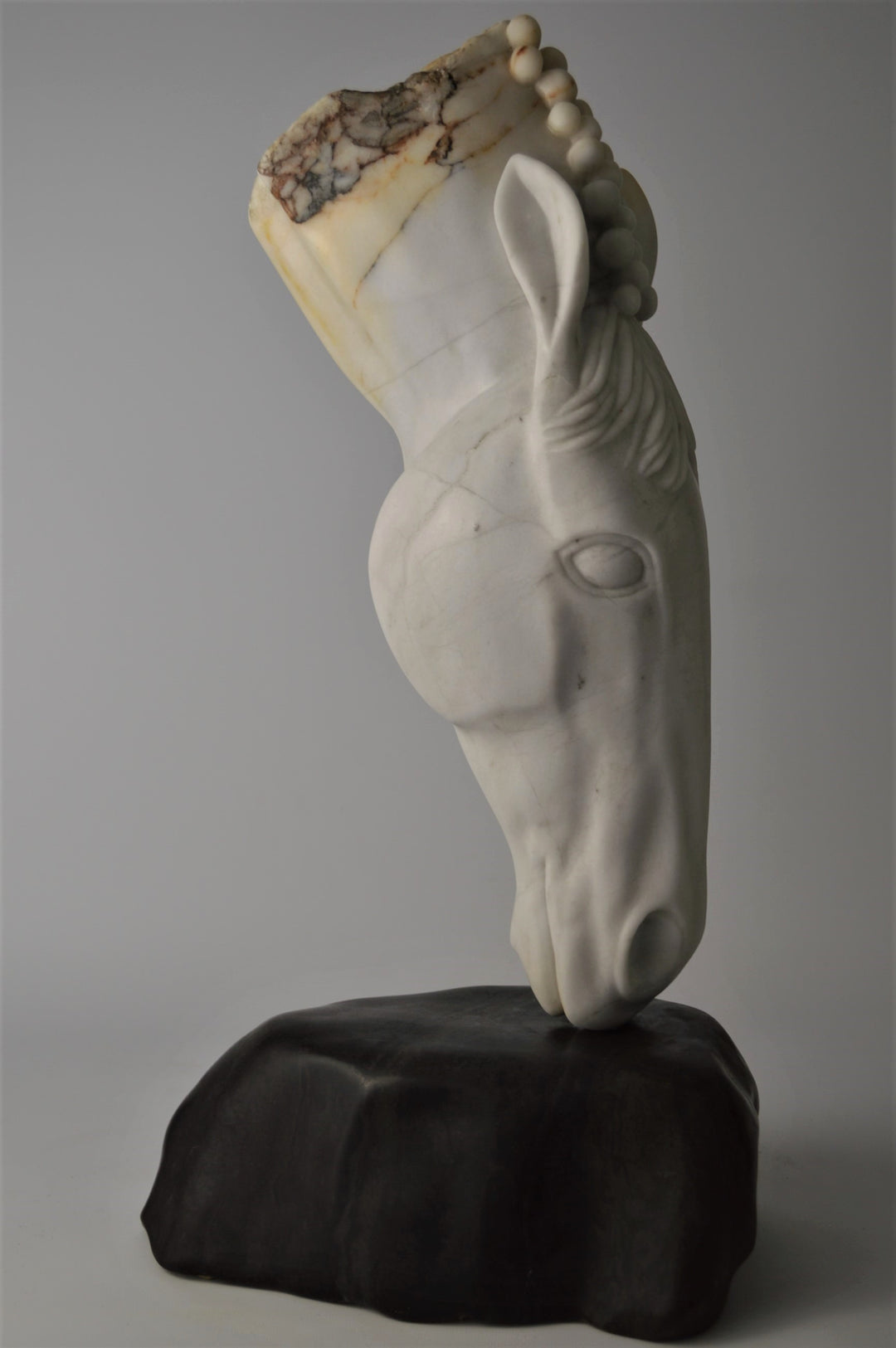 Deborah Harrison sculpture Palomo, a one-off hand-carved horse head in rainbow alabaster with intricate mane detail and a natural crown of rounded alabaster spheres, mounted on a dark soapstone base. The alabaster reveals soft white, ivory, cream and golden brown tones with darker natural veining, blending realism with symbolic form.