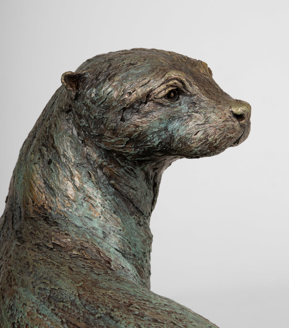 Bronze sculpture of an alert otter perched on a sculpted driftwood log, displayed on a polished black base