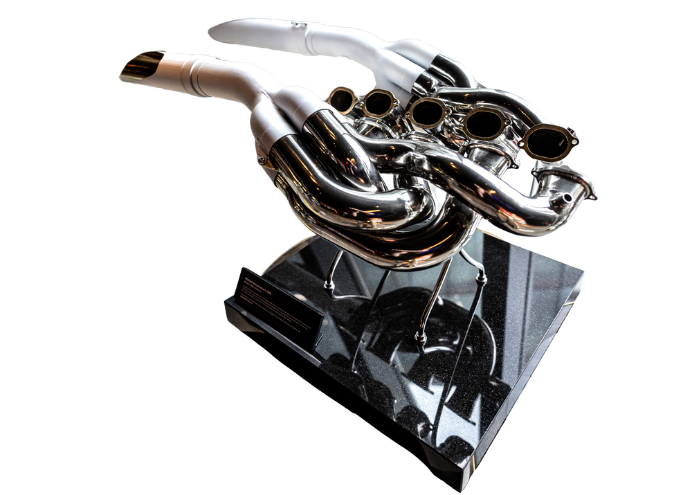 Highly polished sculptural artwork by Mike O’Connor crafted from the authentic race-used exhaust system of Michael Schumacher’s 1995 Benetton B195 Formula One car. The piece features flowing Inconel and stainless-steel pipes with mirror-finished chrome surfaces and 24-karat gold interior detailing, mounted on a sleek stand. A striking one-of-one collector’s piece 