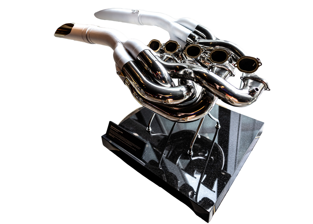 Highly polished sculptural artwork by Mike O’Connor crafted from the authentic race-used exhaust system of Michael Schumacher’s 1995 Benetton B195 Formula One car. The piece features flowing Inconel and stainless-steel pipes with mirror-finished chrome surfaces and 24-karat gold interior detailing, mounted on a sleek stand. A striking one-of-one collector’s piece 