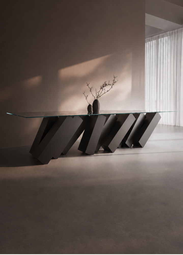 Duffy London Megalith Dining Table with angled black monolithic base and clear glass top, creating a gravity-defying illusion of collapsing architectural forms.