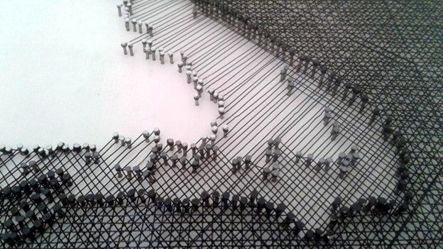 Portrait of John Lennon formed from fine black enamelled copper wire tensioned around thousands of small nails on a white board, with layered linear wiring defining facial features, round glasses and hair through tonal contrast, depth and shadow across a textured monochrome surface.