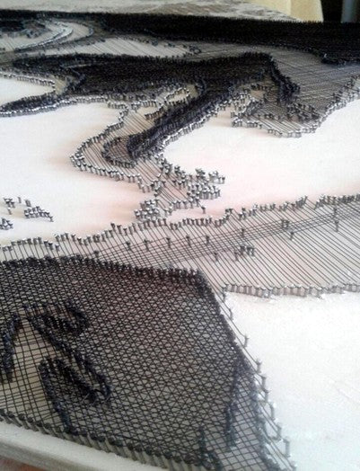 Portrait of John Lennon formed from fine black enamelled copper wire tensioned around thousands of small nails on a white board, with layered linear wiring defining facial features, round glasses and hair through tonal contrast, depth and shadow across a textured monochrome surface.